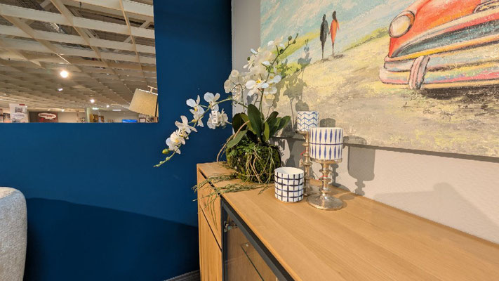 Holz-Sideboard mit Dekoration vor einer blauen Wand und einem Gemälde eines roten Autos.