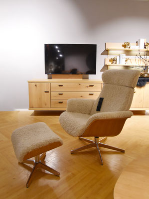 Beiger Sessel mit Schaffell-Bezug und Fußhocker, vor einer Holz-Kommode mit einem Fernseher.