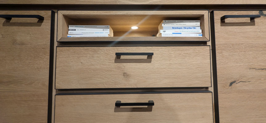 Detailansicht eines hellbraunen Holzschranks mit zwei Schubladen und dunklen Metallgriffen.