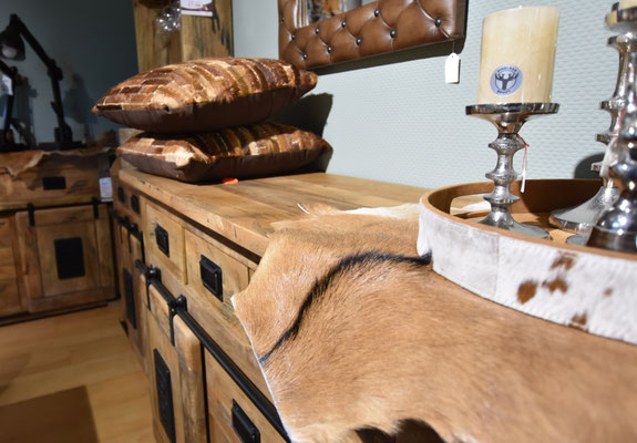 Naheinstellung eines Holz-Sideboards mit Felltuch, Fellkissen und Silberkerzenleuchtern.