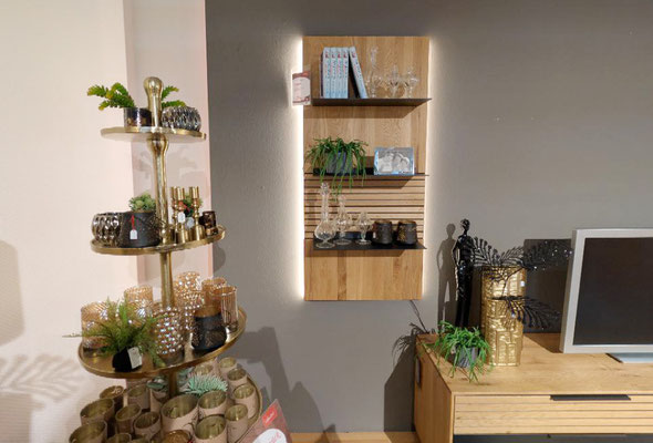 Holzregal mit Beleuchtung, dekoriert mit Glas, Büchern und Pflanzen, neben einem Messingständer.