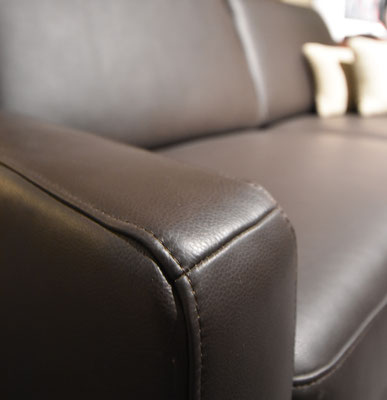 Nahaufnahme der Armlehne eines dunkelbraunen Ledersofas mit Ziernaht.