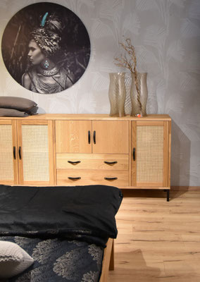Links steht ein Bett mit schwarzer Bettwäsche, dahinter eine Holzkommode.