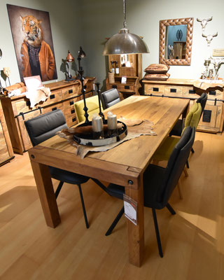 Massiver Holztisch mit schwarzen und gelben Stühlen, rustikalen Möbeln und einem Tigerbild.