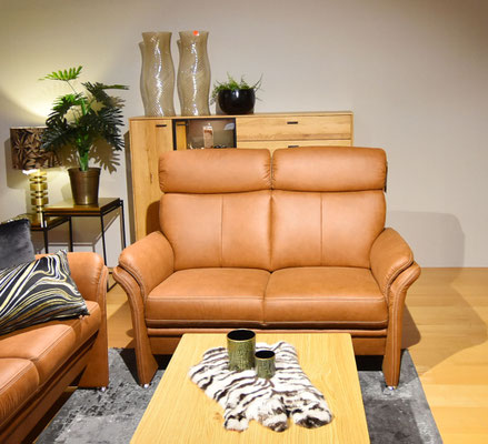 Zweiersofa aus hellbraunem Leder, Couchtisch mit Fell, und Holzschrank mit Deko-Vasen dahinter.