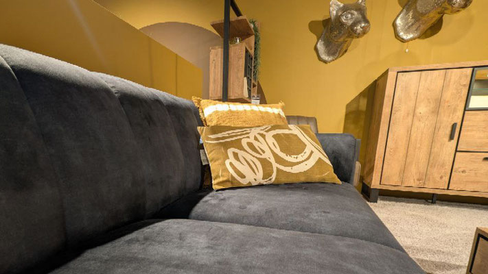 Dunkelgraues Sofa mit zwei gold-gelb gemusterten Zierkissen vor einer gelben Wand.