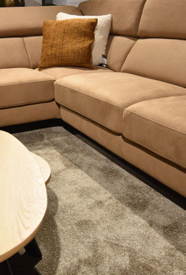 Hellbraunes Leder-Ecksofa mit zwei Zierkissen, davor ein Teppich und Couchtisch.