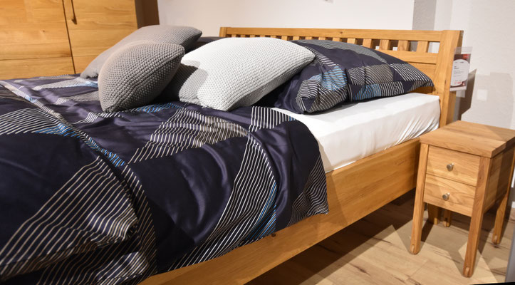 Bett mit Holzrahmen, dunkelblaue gemusterter Bettdecke und verschiedenen Kissen.