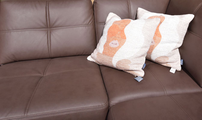 Nahaufnahme eines braunen Ledersofas mit Rückenlehne und dekorativen, gemusterten Kissen.