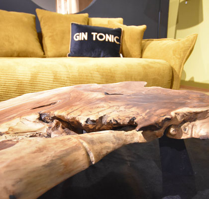 Im Vordergrund ist eine große Holzplatte zu sehen, dahinter steht ein senfgelbes Sofa.