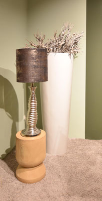 Silberne Tischlampe mit strukturiertem Fuß und dunklem Schirm, neben einer weißen, hohen Vase.