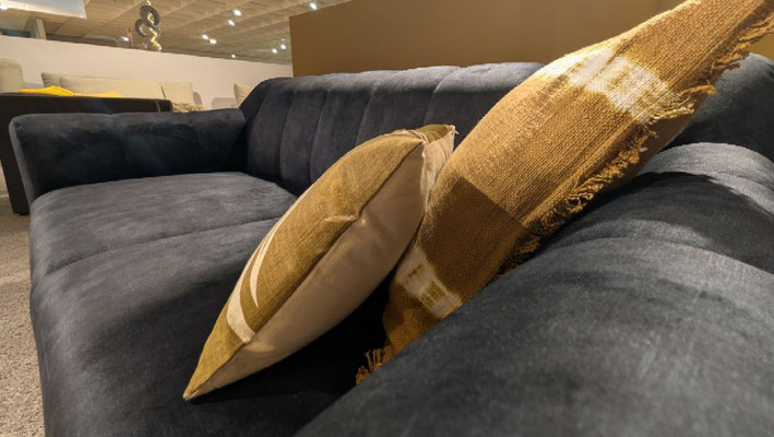 Nahaufnahme eines dunkelgrauen Sofas mit zwei gold-braun gemusterten Zierkissen.