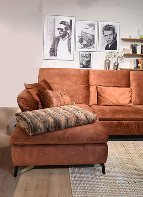 Rustfarbenes Ecksofa mit Pelzdecke, Kissen und gerahmten Schwarz-Weiß-Fotos an der Wand.