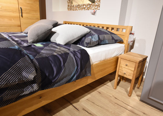 Bett mit Holzrahmen, dunkelblaue gemusterter Bettdecke und verschiedenen Kissen.