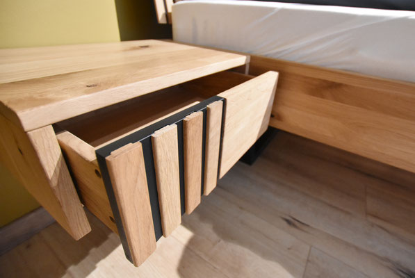 Nahaufnahme eines offenen Nachttischschubfachs aus Holz mit schwarzen, vertikalen Zierelementen.