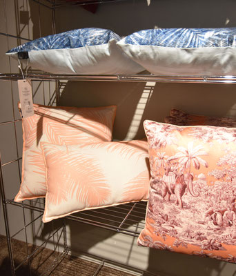 Kissen mit Dschungel-Motiven in Pfirsich und Orange sowie blauen Mustern auf einem Regal.
