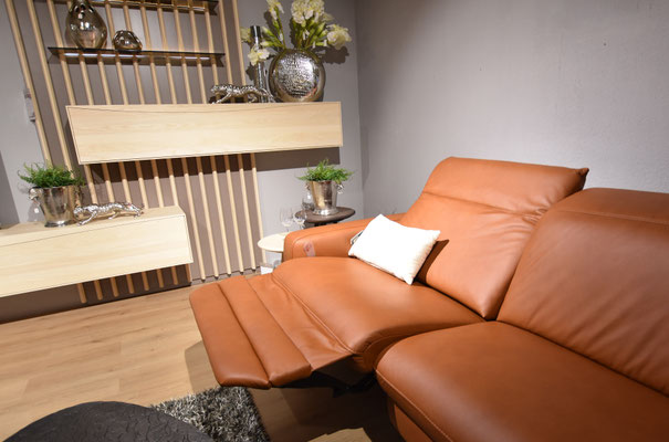Braunes Ledersofa mit Relaxfunktion in einem modernen Wohnzimmer mit Holzpaneelen und Dekoration.