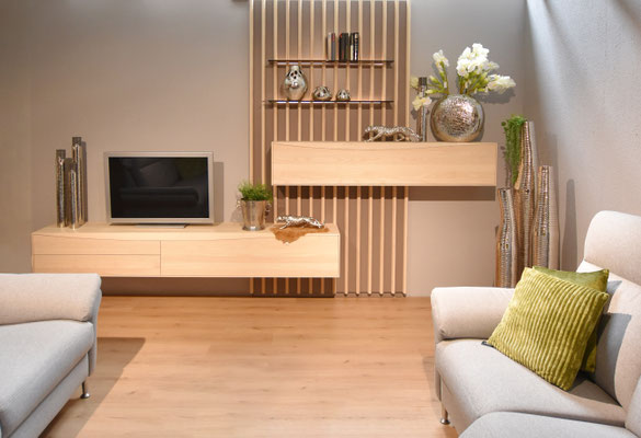 In einem Wohnzimmer stehen links und rechts zwei graue Sofaelemente, dahinter hängen zwei Holz-Sideboards.