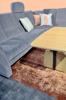 Ein graues Ecksofa mit verschiedenen Kissen, einem Holztisch und einem braunen Teppich.