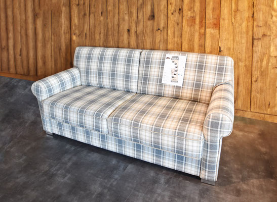 Ein klassisches Zweisitzer-Sofa mit grau-blau-weißem Karomuster vor einer Holzwand.