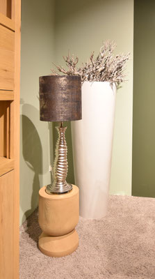 Lampe auf einem hölzernen Beistelltisch neben einem hohen, weißen Topf mit vertrockneten Ästen.