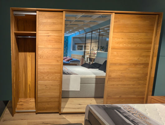 Großer Kleiderschrank aus hellem Holz mit Schiebetüren und zentralem Spiegel.