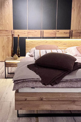 Großes Holzbett mit rosafarbiger Bettwäsche, braunem Kissen und Decke und einem Holznachttisch.