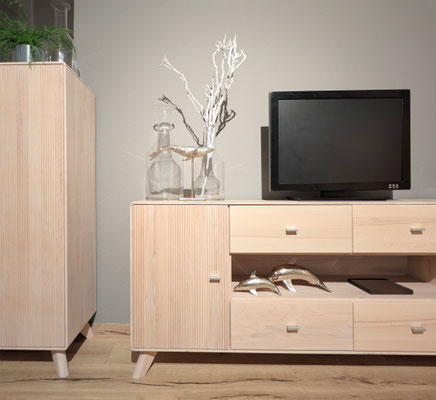 Holzschrank mit TV-Bank, Fernseher, silberner Dekoration und einem Teil eines mintgrünen Sofas.
