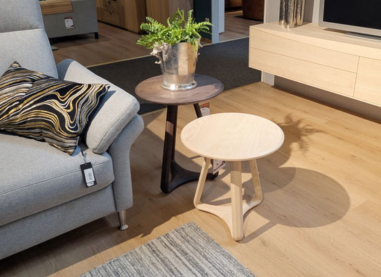 Neben einem grauen Sofa zwei Beistelltische, einer aus Holz, einer aus Granit.