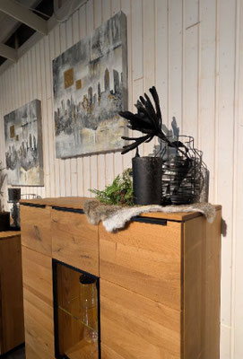 Langes Holz-Sideboard mit schwarzem Griff und Deko. Im Hintergrund eine weiße Holzwand mit Bildern.