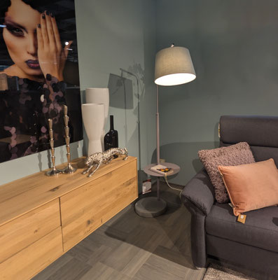 Sideboard aus Holz mit Deko (Vasen, Kerzenständer, Leopardenfigur), Stehlampe und Sessel.