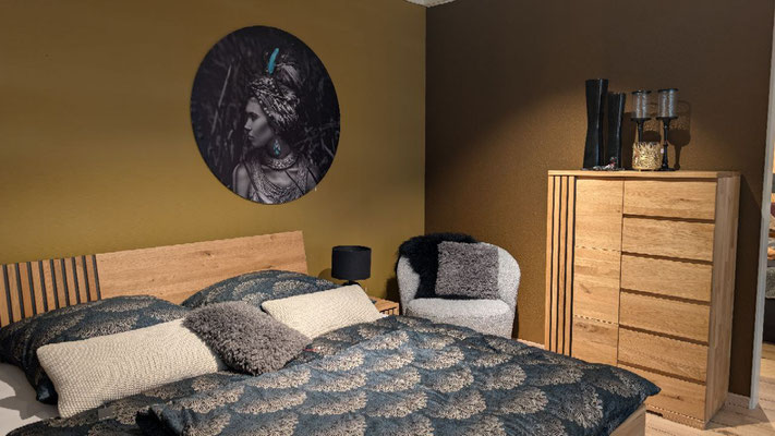 Schlafzimmer mit Holzbett und Nachttisch, davor ein hoher Holzschrank. Wände in Gelbbraun und Braun.