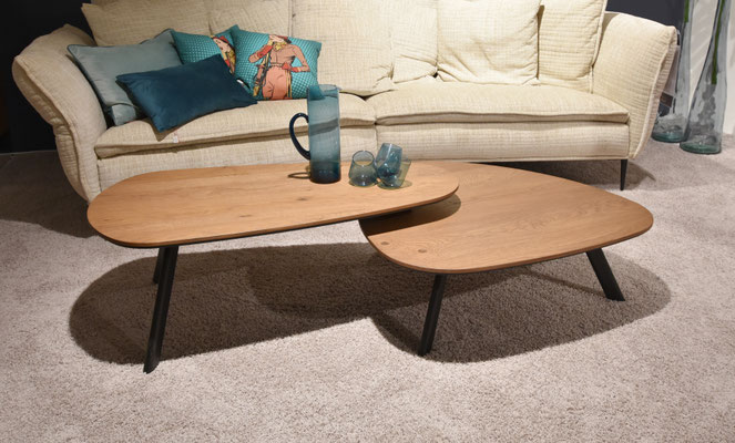 Couchtisch mit zwei organisch geformten Holztischplatten auf schwarzen Beinen vor hellem Sofa.