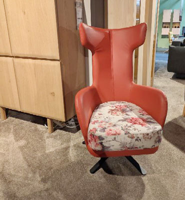 Roter Ohrensessel mit floral gemustertem Sitzkissen steht auf einem Teppich neben einem Holzschrank.