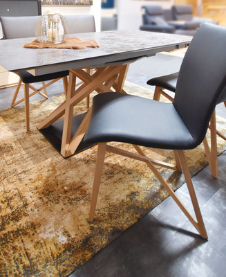 Schwarze Stühle mit hellem Holzgestell an einem dunklen Tisch auf goldenem Teppich.