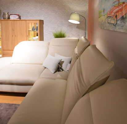 Helles, cremefarbenes Ledersofa in Eckansicht mit weißen Kissen und Stehlampe.