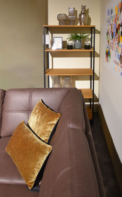 Ein braunes Ledersofa mit goldenen Samtkissen vor einem hellen Holzregal mit schwarzen Akzenten.