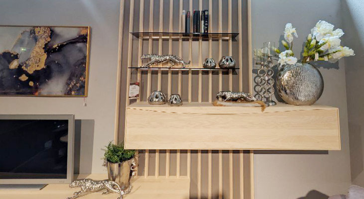 Hängendes Holzregal mit Glasböden vor einer Lamellenwand mit Dekoration.