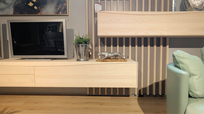 Helle Holz-TV-Bank mit Fernseher, Pflanzen und einer silbernen Leoparden-Figur vor einer Lattenwand.