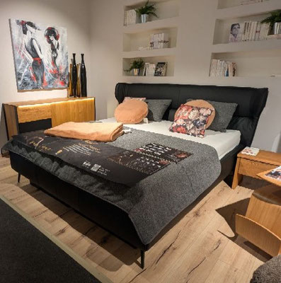Modernes Schlafzimmer mit schwarzem Bett, Holz-Sideboard, Kunst und beleuchteten Wandnischen.