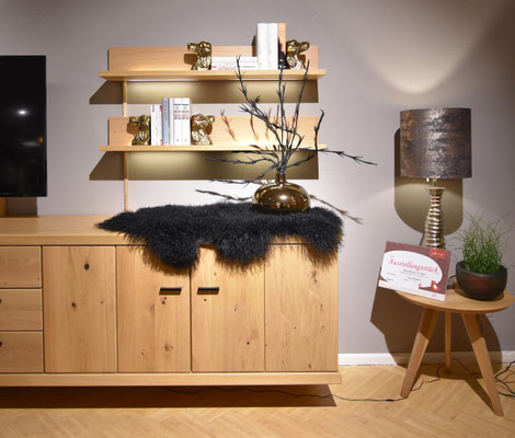 Holz-Sideboard mit schwarzem Lammfell, darüber hängende Holzregale mit Büchern und Deko-Figuren.