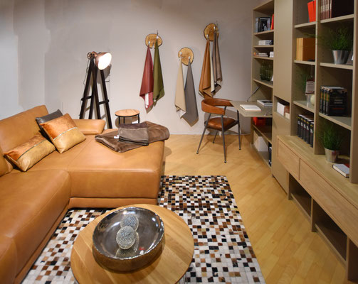 Cognacfarbenes Ledersofa, Couchtisch und beiges Regalwand in modernem Wohnzimmer.