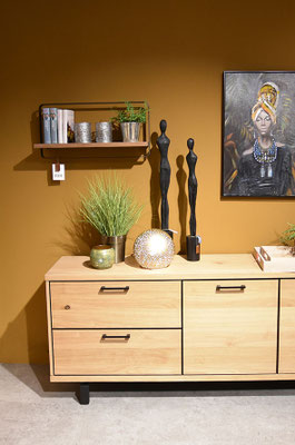 Ein Sideboard aus hellem Holz mit schwarzen Griffen, darauf zwei dunkle Statuetten und Kunstpflanzen.
