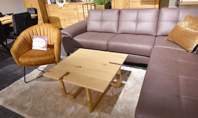 Braunes Leder-Ecksofa und Holztisch neben Sessel auf weißem Teppich.
