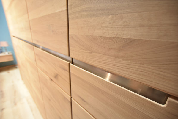 Nahaufnahme einer Holzschrankwand mit geschlossenen Schubladen und Türen und Metallgriffen.
