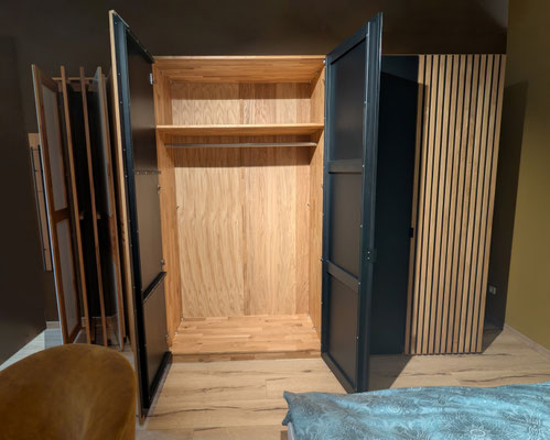 Offener hellbrauner Kleiderschrank mit zwei Fächern, Stange und schwarzen Rahmentüren.