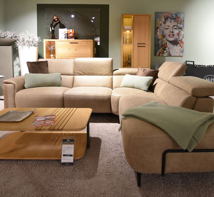 Helle Wohnzimmerecke mit beigefarbenem Ledersofa, Holztisch, flauschigem Teppich und Gemälde.