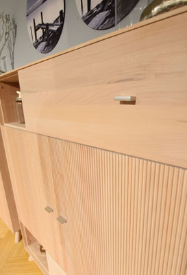 Nahaufnahme heller Holzmöbel mit einer Schublade und Lamellentüren, silberne Griffe.