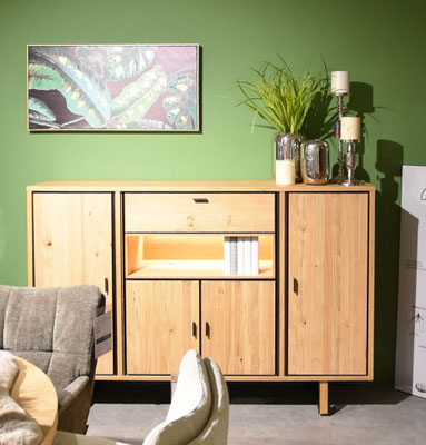Modernes Sideboard aus hellem Holz an einer grünen Wand mit einem Gemälde und Pflanzen.