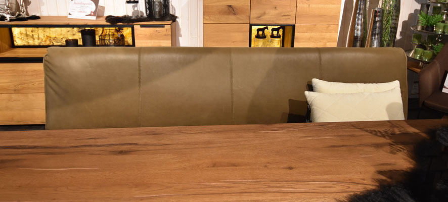 Braune Lederbank mit Holztisch und Holzschränken im Hintergrund. Helle Kissen liegen auf der Bank.